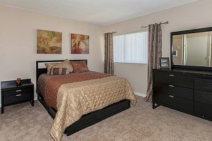 Affordable Apartments for Rent in Long Beach - Seaport Village - Carpeted Bedroom with Cozy Bed, Futon, Dresser, and Window With Shutters